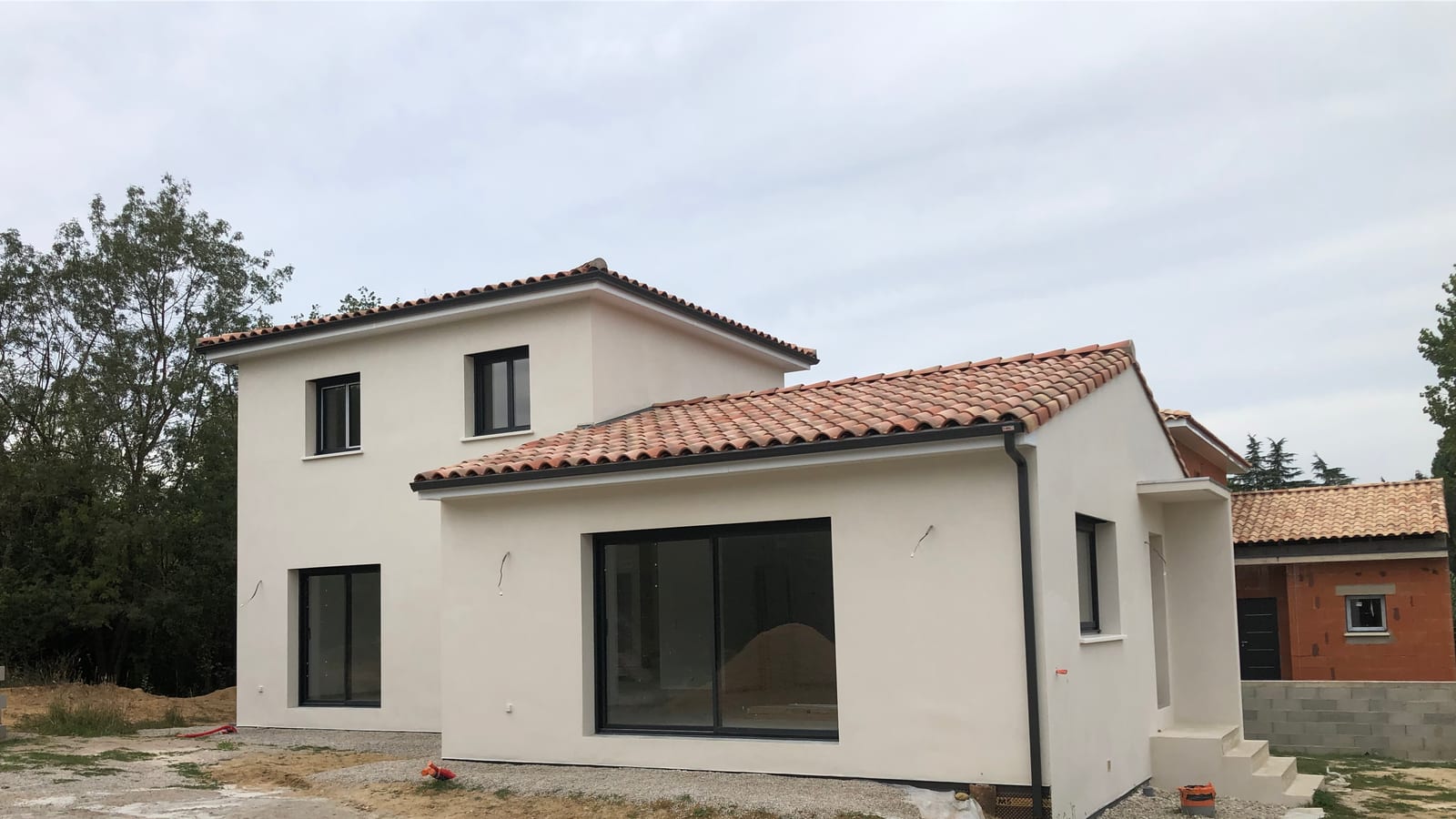 Maison neuve enduite en fin de gros œuvre, parpaings et briques sur le chantier voisin